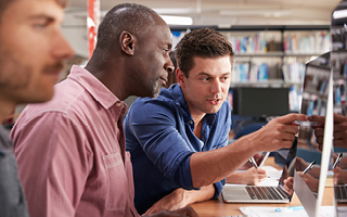 Men In Library Working On Laptops Together