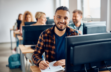 Older student sat in a classroom with desktops smiling at the camera