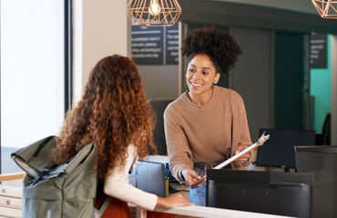 Woman with packback travelling talking to a female clerk smiling 