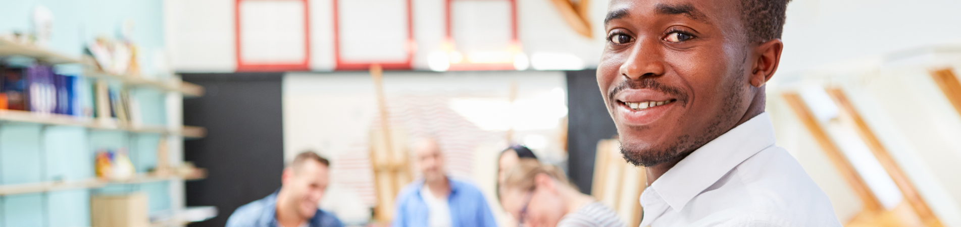 Man smiling at camera with colleagues working in background