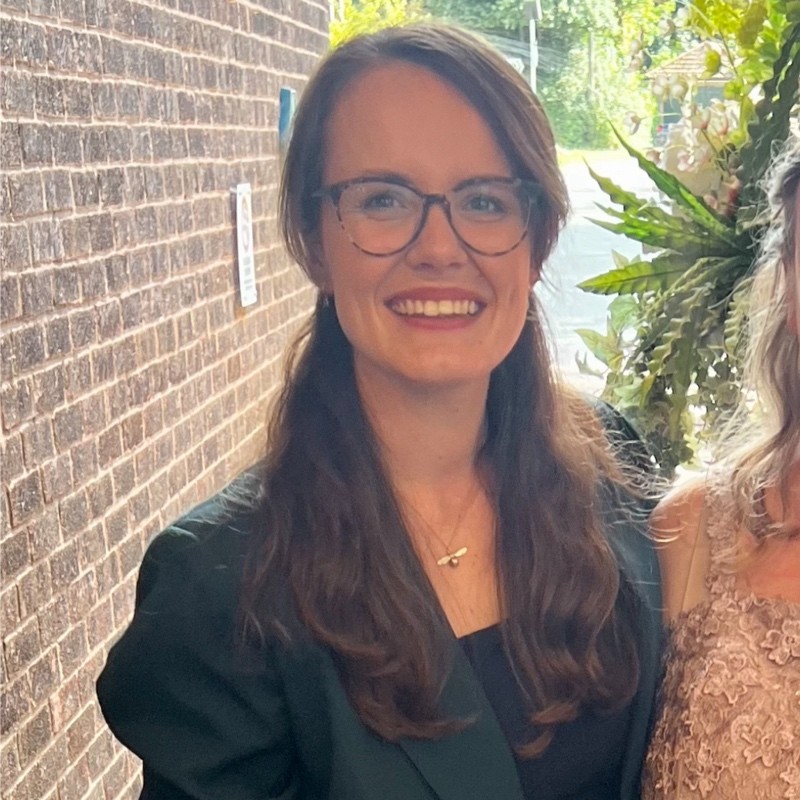 Brown hair lady with glasses in a black blazer smiling