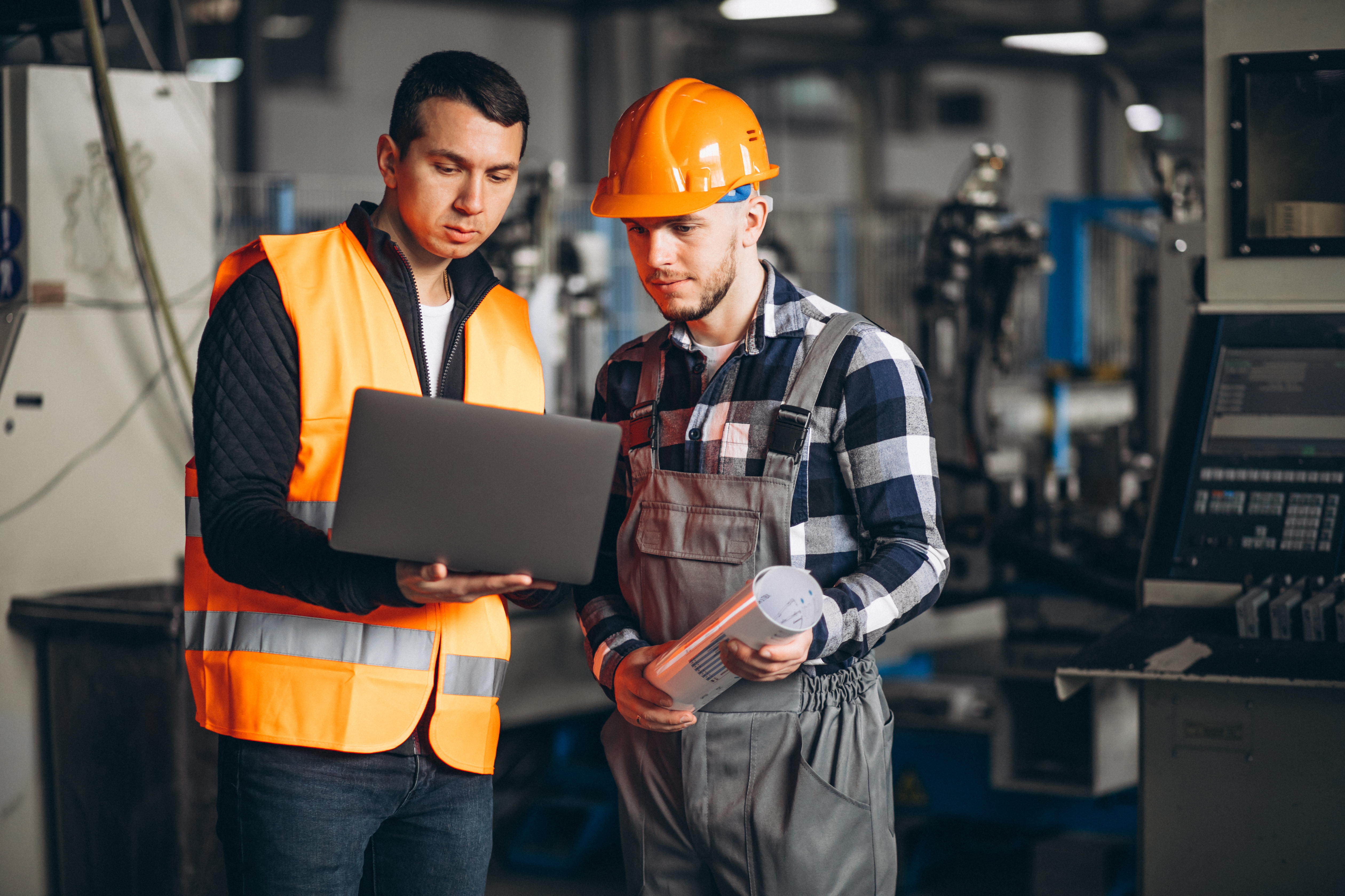 Two male contruction workers wearing high vis and hard hat looking at a laptop